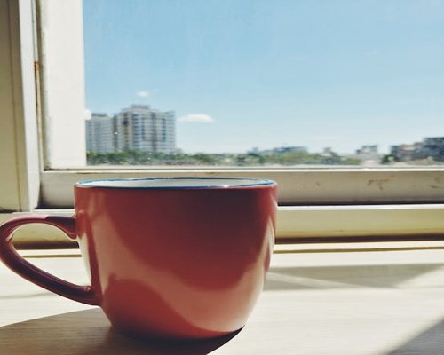 Person relaxing comfortably with a coffee mug near a sunny window in Jakarta apartment