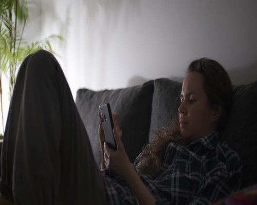 A person resting on a comfortable sofa, looking away from their smartphone screen